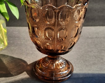 May include: A brown glass pedestal bowl with a scalloped rim and a textured surface. The bowl has a wide base and a narrow top.