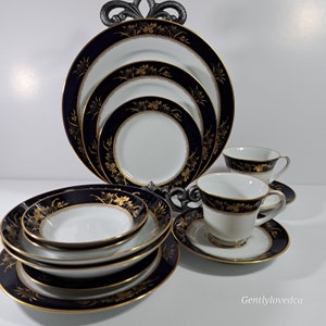 May include: Elegant navy blue and gold china set. The set includes various sized plates, bowls, teacups, and saucers. Each piece features a navy blue border with gold floral accents and gold trim. The china is displayed on a decorative metal stand.