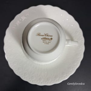 K&ouml;nnte beinhalten: Wei&szlig;es Teetassen- und Untertassen-Set aus Knochenporzellan mit einem goldenen, gepr&auml;gten Blumenmuster. Auf der Unterseite der Tasse steht "Bone China mikasa&reg;  NARUMI - JAPAN WHITE SILK A 7050"