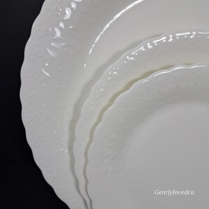 K&ouml;nnte beinhalten: Set aus drei wei&szlig;en Keramik-Dinnertellern mit einem erhabenen, strukturierten Design. Die Teller sind &uuml;bereinander gestapelt, wobei der gr&ouml;&szlig;te Teller unten und der kleinste Teller oben liegt.