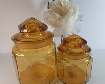 May include: Two amber glass canisters with lids. The canisters are octagonal in shape and have a vintage look.