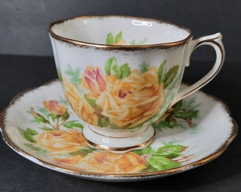 May include: A white teacup and saucer set with a yellow rose floral pattern and gold trim.