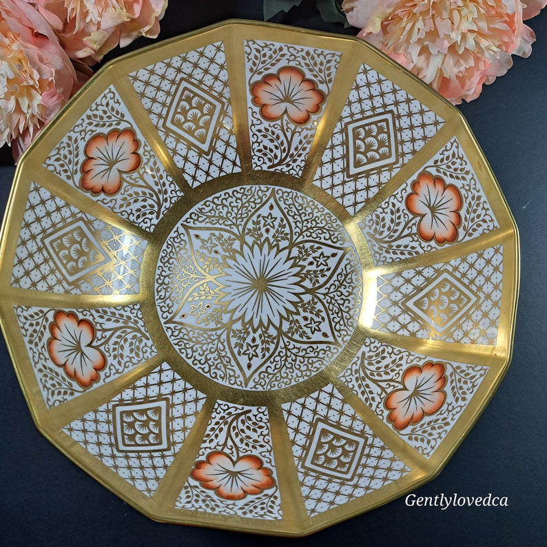 May include: A white porcelain bowl with a gold and orange floral design. The bowl has a scalloped edge and is decorated with a repeating pattern of flowers and leaves.