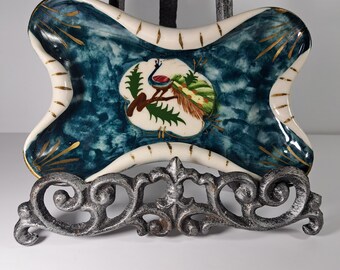 May include: A blue and white ceramic dish with a gold trim and a peacock design. The dish is on a metal stand.