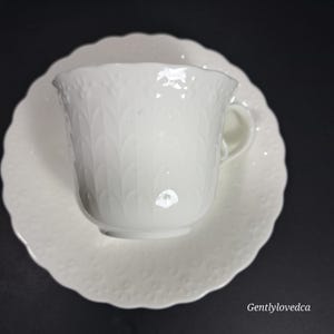 K&ouml;nnte beinhalten: Wei&szlig;es Porzellan-Teetassen- und Untertassen-Set mit einem erhabenen Blumendesign. Die Tasse hat einen gewellten Rand und einen zarten Griff.