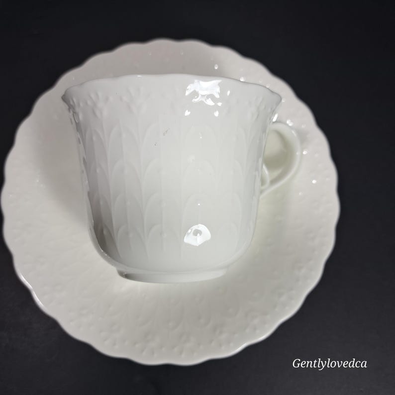 K&ouml;nnte beinhalten: Wei&szlig;es Porzellan-Teetassen- und Untertassen-Set mit einem erhabenen Blumendesign. Die Tasse hat einen gewellten Rand und einen zarten Griff.