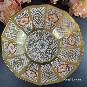May include: A white and gold octagonal serving bowl with a floral design and intricate gold detailing. The bowl has a scalloped edge and a raised center.