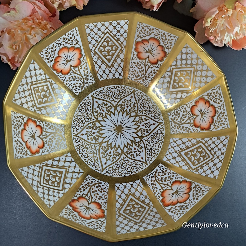 May include: A white and gold octagonal serving bowl with a floral design and intricate gold detailing. The bowl has a scalloped edge and a raised center.