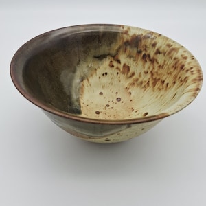 Peut inclure: Un bol en céramique fait à la main avec un design tacheté et terreux. Le bol présente un dégradé de couleurs, passant d'un bord marron foncé à un intérieur beige avec des mouchetures marron. Le bol est idéal pour servir des aliments.