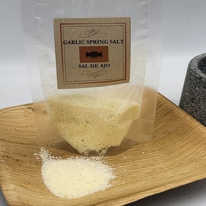May include: A clear plastic pouch with a zip closure containing a white powder labelled "Garlic Spring Salt" and "Sal de Ajo".