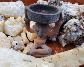 May include: A small terracotta figurine of a person holding a bowl, surrounded by white and brown resin pieces on a brown surface.