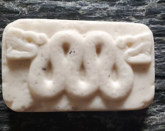 Könnte beinhalten: Eine weiße Seifenstange mit einem erhabenen Design einer Schlange mit zwei Köpfen. Die Schlange ist zu einem Kreis zusammengerollt und hat eine strukturierte Oberfläche.