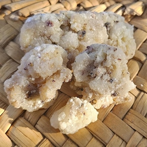 May include: Close-up of a cluster of white, crystalline resin with brown flecks, resting on a woven basket surface.