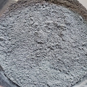 May include: A close-up view of a pile of gray powder. The powder is fine and has a slightly textured surface.