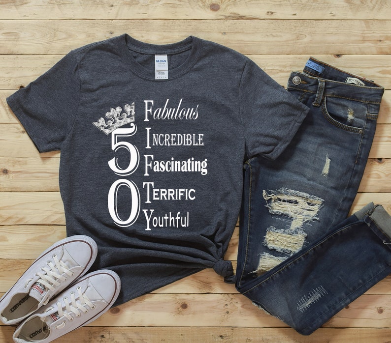 May include: A dark gray t-shirt with a white graphic that says "50" with a crown above the number. The graphic also includes the words "Fabulous, Incredible, Fascinating, Terrific, Youthful".