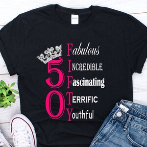 May include: Black t-shirt with a pink number 50 and the words "Fabulous, Incredible, Fascinating, Terrific, Youthful" written vertically. A silver crown is above the number 50.