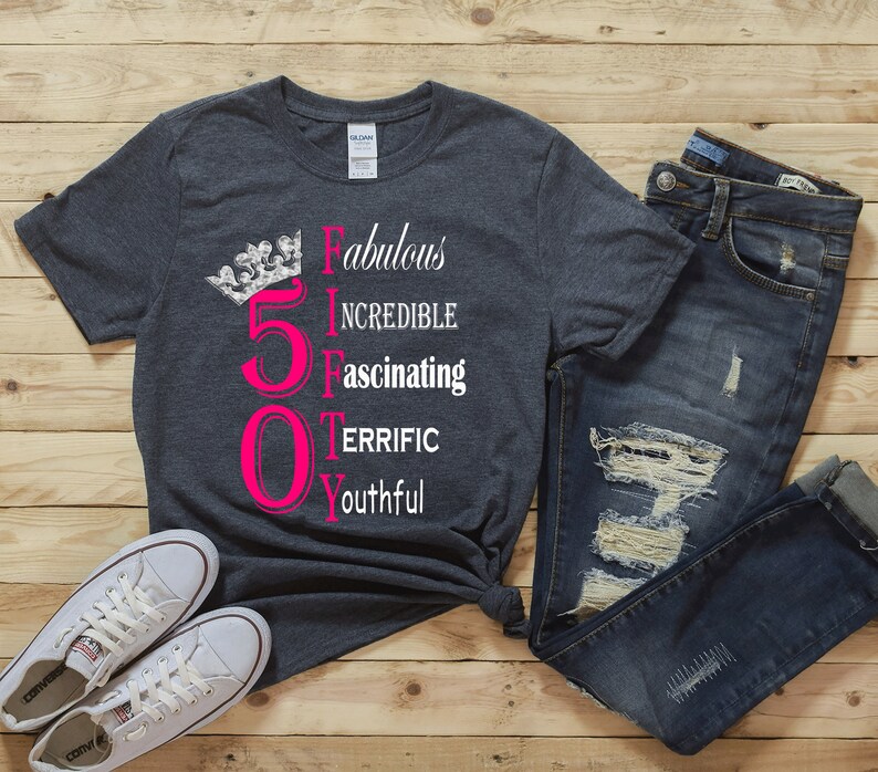 May include: A dark grey t-shirt with a pink number 50 and a silver crown. The text "Fabulous, Incredible, Fascinating, Terrific, Youthful" is written vertically next to the number.