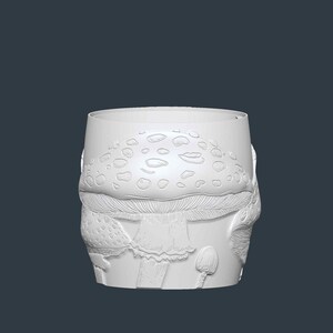 May include: A white, cylindrical container with a detailed mushroom design. The design includes a mushroom cap with spots, a stem, and smaller mushroom illustrations. The container is likely made of ceramic or a similar material.