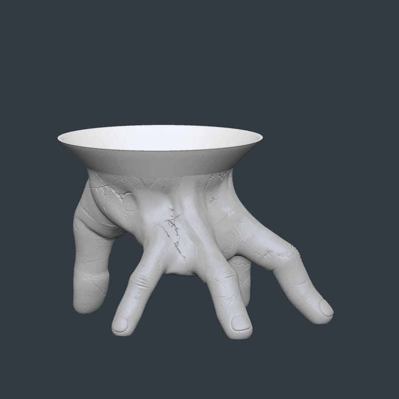 May include: A white, hand-shaped decorative bowl with a wide, shallow opening. The bowl is supported by a detailed, textured hand with visible veins and cracks, creating a unique and artistic design. The background is a solid, dark gray.
