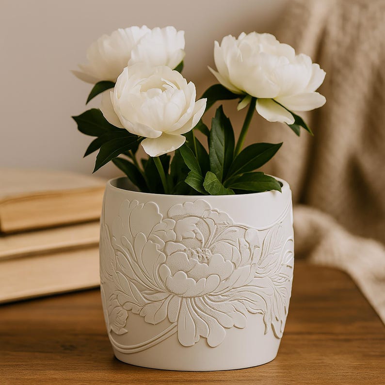 May include: A white ceramic flower pot with an embossed peony design, holding several white peony blooms with green leaves. The pot sits on a wooden surface, creating a natural and elegant aesthetic.