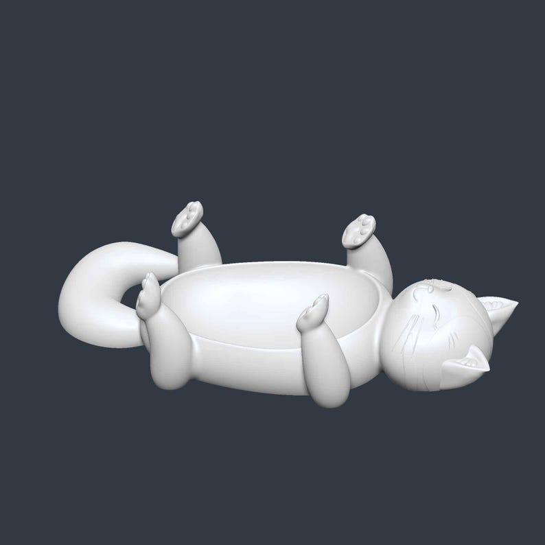 May include: A white cat-shaped decorative bowl, lying on its back with its paws and tail curved. The bowl has a rounded shape, with the cat's face and whiskers detailed on one end. The cat is in a relaxed pose.