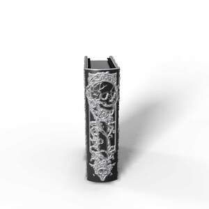 May include: A black book with silver embellishments. The cover features a skull design and ornate floral patterns. The book is standing upright against a white background.