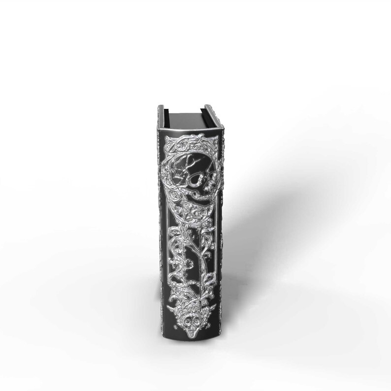 May include: A black book with silver embellishments. The cover features a skull design and ornate floral patterns. The book is standing upright against a white background.