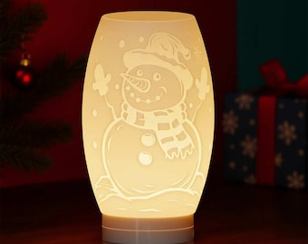 May include: A glowing, off-white ceramic lamp with a snowman design. The snowman wears a hat and scarf, with snowflakes and a smiling face. The lamp is cylindrical with a rounded top and base, perfect for holiday decor.