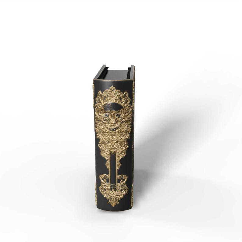 May include: A black book with gold embellishments featuring a skull design. The cover has ornate, detailed patterns and a skull in the center. The book is upright, with a shadow cast to the right.