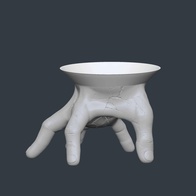 May include: A white, hand-shaped decorative bowl. The bowl's base is formed by a hand with fingers extended, supporting a circular, shallow dish. The surface has a textured, cracked appearance. The background is a solid, dark gray.