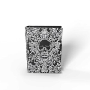 May include: A black and silver decorative book with a skull design. The cover features a detailed silver skull and ornate floral patterns. The book has a gothic or fantasy theme.