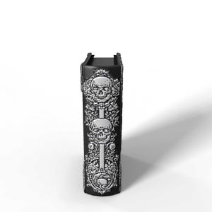 May include: A black, rectangular decorative box with silver skull and floral relief designs. The box features two skulls and floral patterns. The top of the box has a rectangular opening.