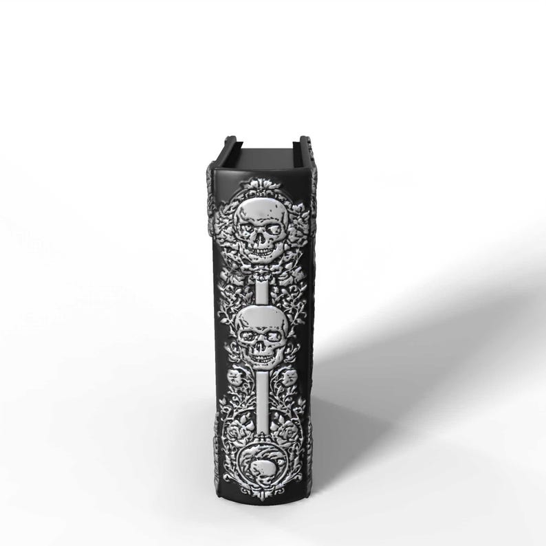 May include: A black, rectangular decorative box with silver skull and floral relief designs. The box features two skulls and floral patterns. The top of the box has a rectangular opening.