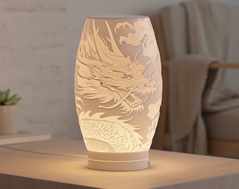 May include: A white ceramic lamp with a detailed dragon design carved into its surface. The lamp has an oval shape and sits on a round base. The dragon is depicted with intricate scales and flowing details.