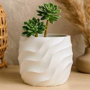 Puede incluir: Una maceta de cerámica blanca con textura de ondas que contiene dos suculentas verdes. La maceta tiene un diseño moderno con una superficie lisa y curvada. Las suculentas tienen hojas verdes vibrantes, creando una estética minimalista.