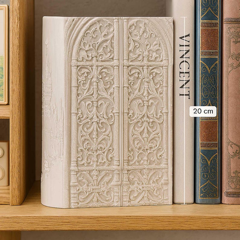 K&ouml;nnte beinhalten: Cremefarbener Buchst&uuml;tze mit einem detaillierten Relief von verzierten Doppelt&uuml;ren. Die Buchst&uuml;tze befindet sich neben einem Buch mit dem Namen "VINCENT" und einem Etikett mit einer H&ouml;he von 20 cm. Die Buchst&uuml;tze steht auf einem Holzregal.