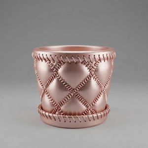 May include: A rose gold planter with a quilted diamond pattern across the exterior surface. The design features raised, stitched-style detailing along the edges of each diamond shape and a matching circular base tray at the bottom.