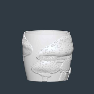 May include: A white ceramic tumbler with a detailed relief of mushrooms. The design features several mushroom caps with textured surfaces and dotted patterns. The tumbler has a cylindrical shape and a smooth, unadorned rim.