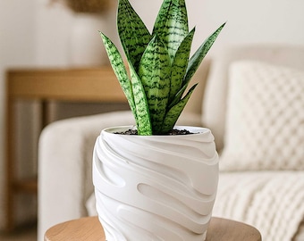 May include: A potted snake plant with green and yellow striped leaves. The plant is in a white ceramic pot with a textured, wave-like design. The pot sits on a small, round wooden table, with a neutral-toned background.