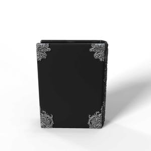 May include: A black book with ornate silver corner accents. The book has a rectangular shape and a smooth, dark surface. The corners feature detailed, decorative designs.
