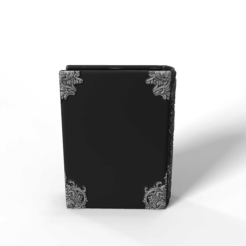 May include: A black book with ornate silver corner accents. The book has a rectangular shape and a smooth, dark surface. The corners feature detailed, decorative designs.
