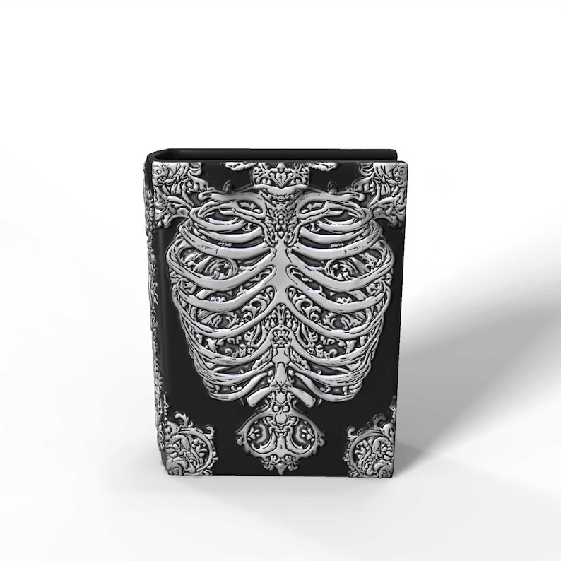 May include: A black box with a detailed silver-colored rib cage design on the front. The sides and top of the box feature ornate, swirling patterns. The overall aesthetic is gothic and decorative.