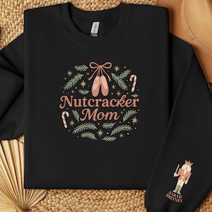 May include: Black sweatshirt with a circular design featuring ballet shoes, candy canes, and the words "Nutcracker Mom." The sleeve displays a Nutcracker soldier graphic with the name "Sarah Britney."