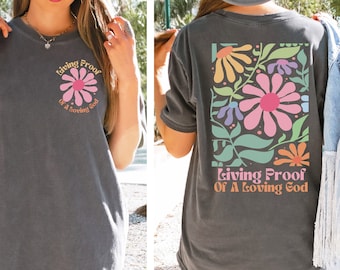 May include: A dark gray t-shirt with a floral design and the text "Living Proof of a Loving God" on the back. The front of the shirt has a smaller floral design and the same text.