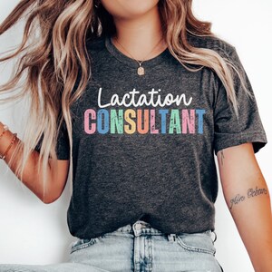 May include: A dark grey t-shirt with the text "Lactation CONSULTANT" in rainbow colors. The text has a distressed, vintage look.