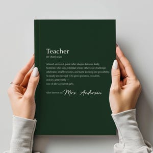 May include: A dark green notebook with the definition of "Teacher" printed in white. The definition includes the text "A heart-centered guide who shapes futures daily." The notebook is personalized with the name "Mrs. Anderson".