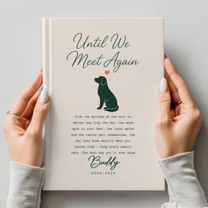 May include: A cream-colored hardcover book featuring the dark green text Until We Meet Again, a dark green silhouette of a dog, a small red heart, and a memorial poem for a dog named Buddy with the dates 2004-2024 printed in dark green.