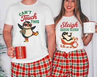 May include: Matching white t-shirts with penguin graphics and text. One shirt says "Can't Touch This" and the other says "Sleigh Queen Sleigh". Both shirts are paired with red plaid pajama pants. Each person holds a mug.