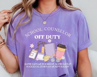 May include: Purple t-shirt with the text "School Counselor Off Duty" and a graphic of school supplies, including a coffee cup, a notebook, a pencil, and a pair of glasses. The text below the graphic reads "Some days we rocked it, some days it rocked us, either way we kept rockin'."