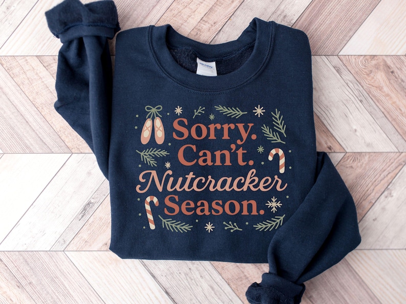 Pu&ograve; includere: Felpa blu navy con la scritta "Sorry, Can't, Nutcracker Season". Il design include scarpette da ballo, bastoncini di zucchero e fiocchi di neve nei toni del marrone e del verde. Un capo festivo e confortevole.